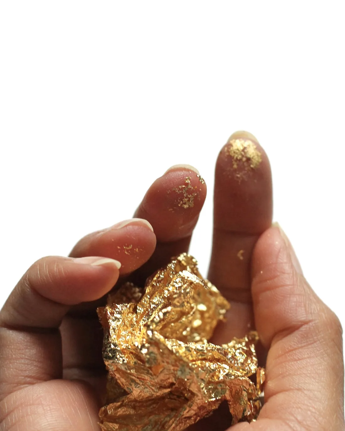 Hoja de pan de oro arrugada sostenida entre los dedos, con restos de oro adheridos a la piel